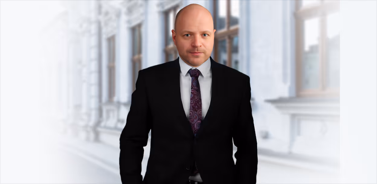 Adwokat Adam Bratkowski w koszuli i krawacie, trzymający marynarkę na ramieniu, na tle rozmytego budynku sądu i grafiki przedstawiającej wagę sprawiedliwości.