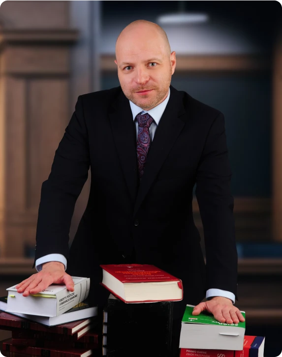 Adwokat Adam Bratkowski w garniturze, stojący przy stole z prawniczymi książkami, na tle wnętrza kancelarii.